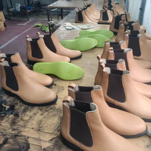 Unfinished Daniele Chelsea Boots lined up on a workbench during the production process at Devogue Paris, showing natural leather upper and elastic gussets before final finishing.