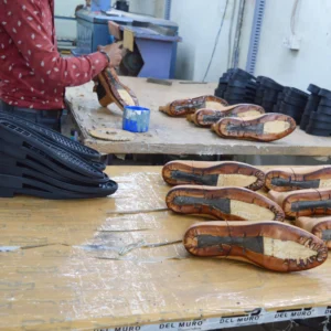 Devogue Paris artisan working on the sole pasting process, showing stitched leather uppers prepared for sole attachment in the shoemaking workshop.